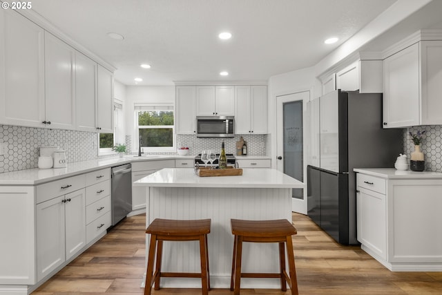 kitchen with appliances with stainless steel finishes, decorative backsplash, white cabinetry, a breakfast bar area, and a kitchen island