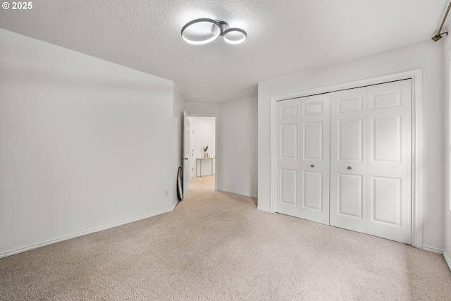 unfurnished bedroom featuring carpet floors, a textured ceiling, a closet, and baseboards