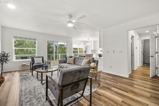living area with a chandelier, a textured ceiling, ceiling fan, wood finished floors, and baseboards