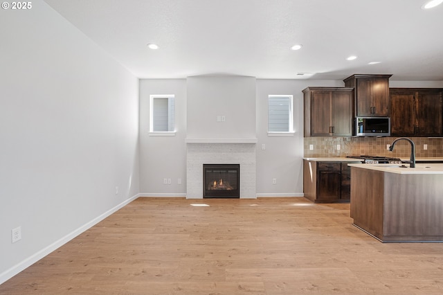 195 SE Acacia Dr, Gresham, OR 97080 - kitchen featuring stainless steel microwave, dark brown cabinets, backsplash, light countertops, and light wood-style flooring