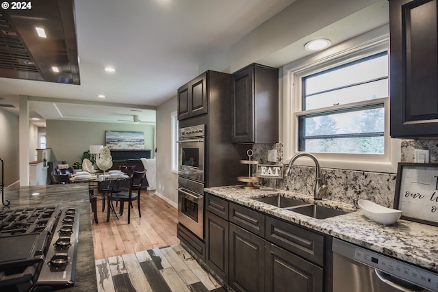 kitchen with a sink, appliances with stainless steel finishes, decorative backsplash, light stone countertops, and light wood finished floors