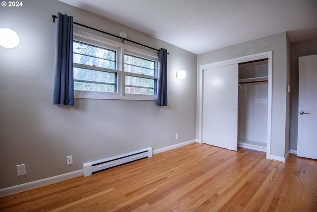 unfurnished bedroom with light wood-type flooring, a baseboard radiator, baseboards, and a closet