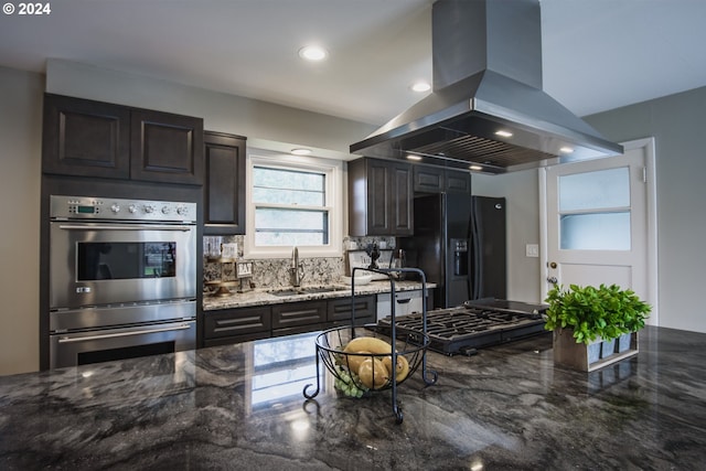 kitchen with island exhaust hood, double oven, a sink, dark stone counters, and black fridge