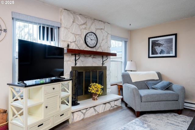 living room with a stone fireplace, a textured ceiling, and hardwood / wood-style flooring