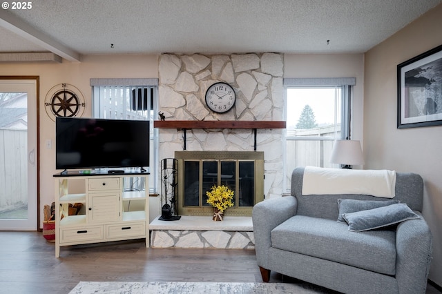 living room featuring wood-type flooring, a textured ceiling, a stone fireplace, and beamed ceiling