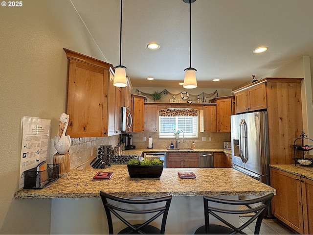 kitchen with a sink, tasteful backsplash, appliances with stainless steel finishes, a peninsula, and brown cabinetry