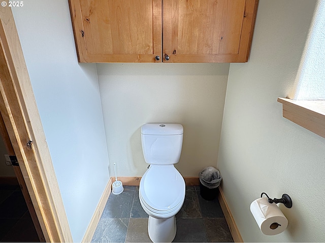 bathroom featuring stone tile flooring, toilet, and baseboards