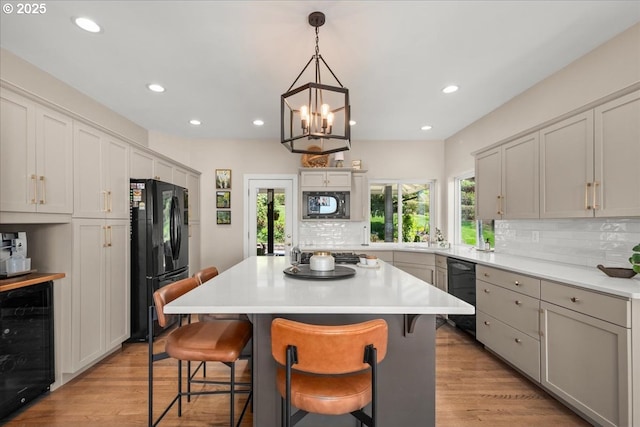 kitchen with black appliances, light wood-style floors, decorative backsplash, and beverage cooler