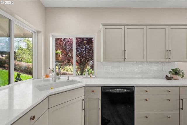 kitchen with tasteful backsplash, light countertops, dishwasher, and a sink