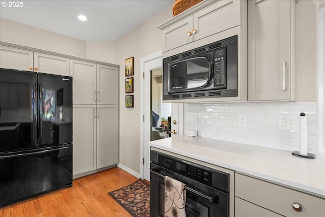 kitchen featuring gray cabinets, tasteful backsplash, light countertops, black appliances, and light wood-type flooring