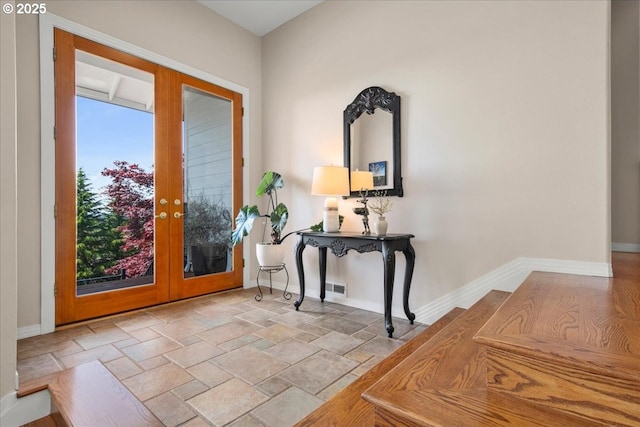 foyer with stone tile flooring, french doors, and baseboards