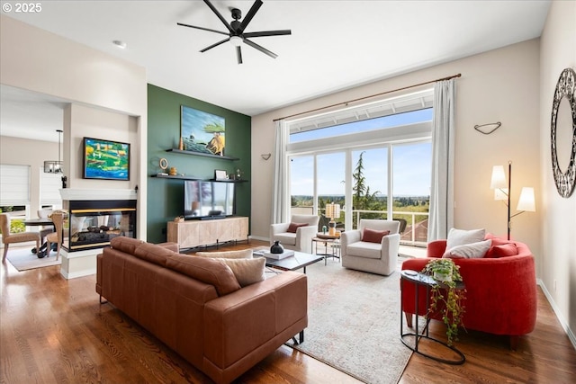 living area featuring wood finished floors, a ceiling fan, a multi sided fireplace, and baseboards