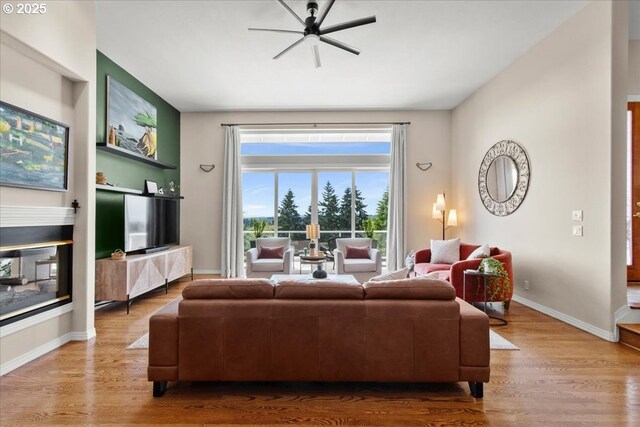 living room featuring baseboards, a glass covered fireplace, wood finished floors, a ceiling fan, and built in shelves