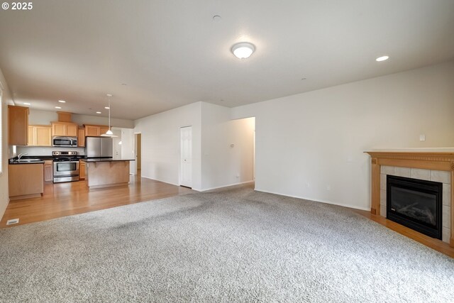 unfurnished living room with a tiled fireplace, light colored carpet, light wood-type flooring, a sink, and recessed lighting