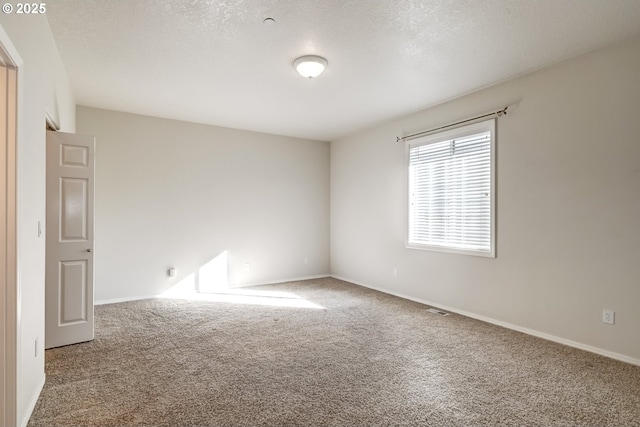 empty room with carpet flooring, a textured ceiling, and baseboards