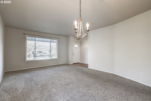 empty room with dark colored carpet, baseboards, and an inviting chandelier