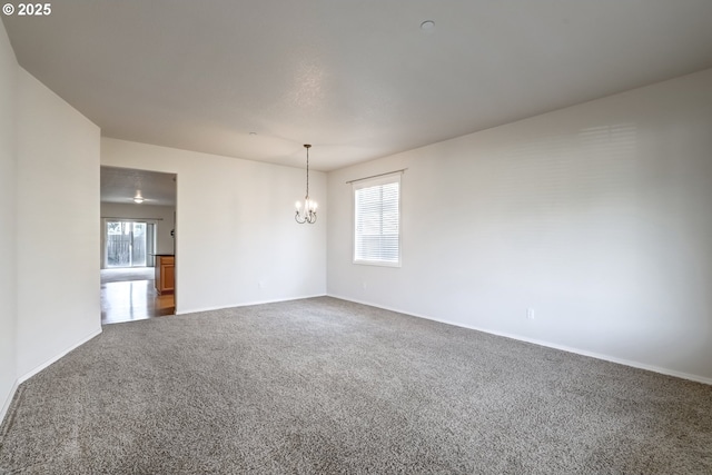 spare room featuring carpet floors, a wealth of natural light, and a notable chandelier