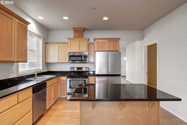 kitchen featuring light brown cabinetry, appliances with stainless steel finishes, a kitchen bar, and a sink