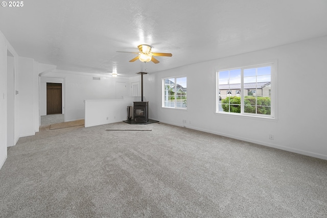 276 S 21st St, Reedsport, OR 97467 - unfurnished living room featuring a wood stove, ceiling fan, carpet floors, and baseboards