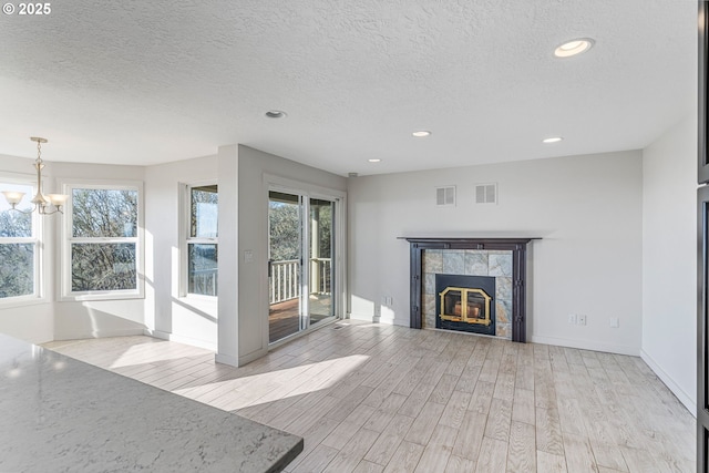 unfurnished living room featuring light hardwood / wood-style flooring, a fireplace, a chandelier, and a healthy amount of sunlight