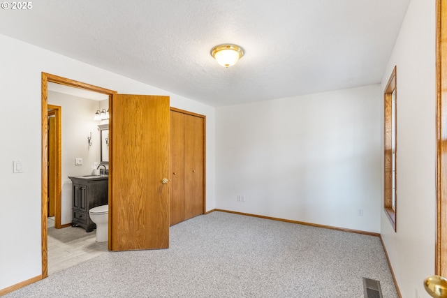 bedroom with connected bathroom, sink, light carpet, a textured ceiling, and a closet