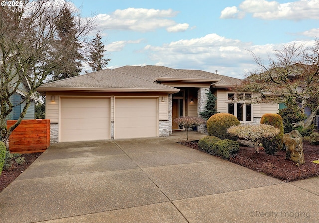 prairie-style home with stone siding, roof with shingles, an attached garage, and driveway