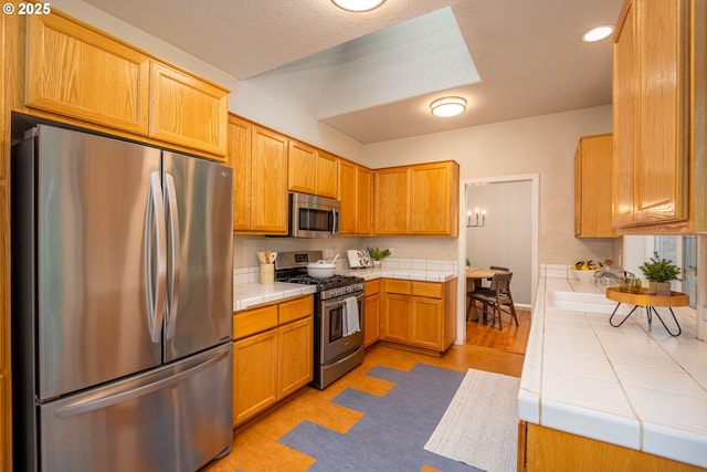 kitchen featuring a textured ceiling, appliances with stainless steel finishes, a sink, and tile counters