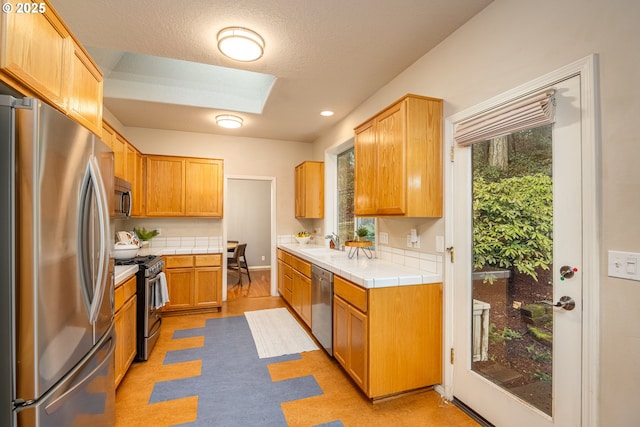 kitchen with tile countertops, a textured ceiling, a skylight, a sink, and appliances with stainless steel finishes