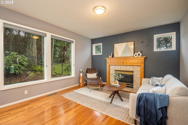 living area with a textured ceiling, a tile fireplace, wood finished floors, visible vents, and baseboards