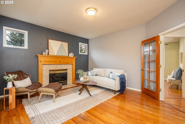 living room with a tiled fireplace, baseboards, and wood finished floors