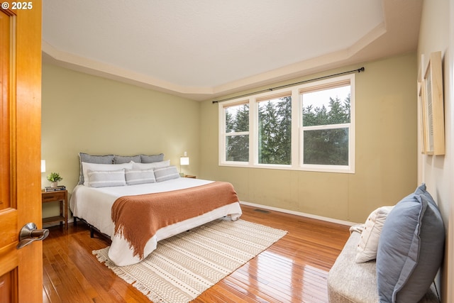 bedroom featuring a tray ceiling, wood finished floors, visible vents, and baseboards