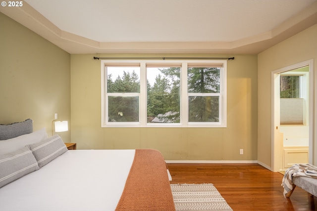 bedroom with ensuite bath, wood finished floors, and baseboards