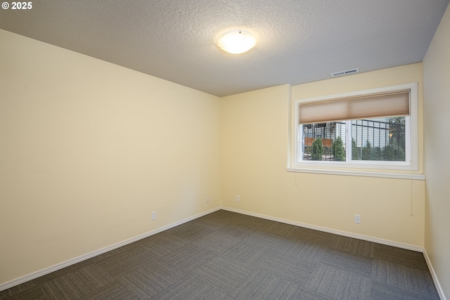 empty room featuring visible vents, dark carpet, a textured ceiling, and baseboards