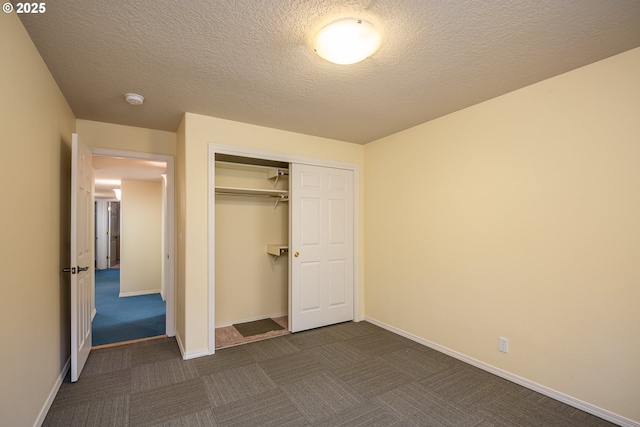 unfurnished bedroom featuring a textured ceiling, a closet, dark carpet, and baseboards