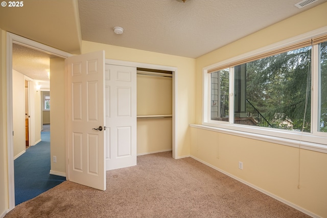 unfurnished bedroom with a textured ceiling, visible vents, baseboards, a closet, and carpet