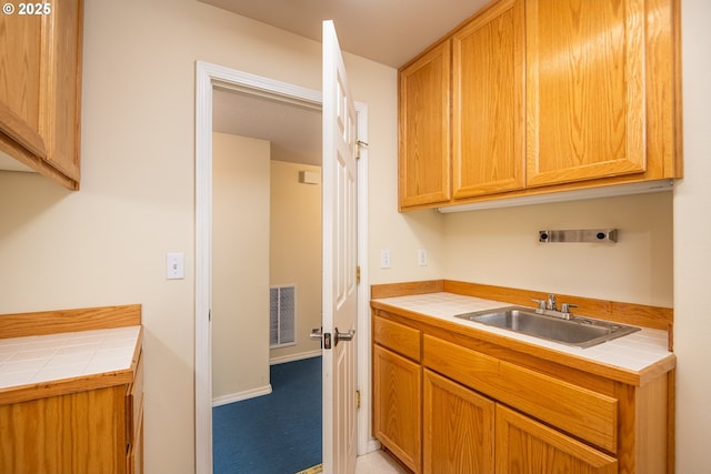 kitchen featuring tile countertops, a sink, and visible vents