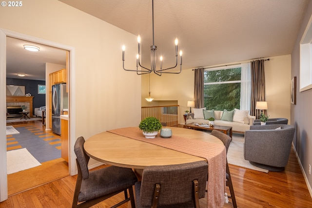 dining space featuring an inviting chandelier, a tiled fireplace, baseboards, and wood finished floors