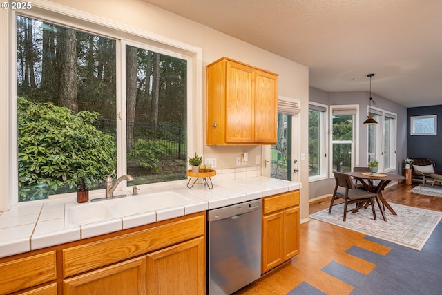 kitchen featuring tile countertops, a sink, baseboards, hanging light fixtures, and dishwasher