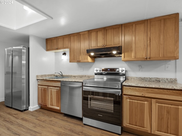 kitchen with brown cabinets, wood finished floors, a sink, under cabinet range hood, and stainless steel appliances