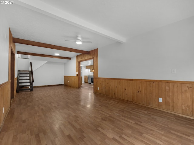 unfurnished living room with beamed ceiling, wainscoting, wood walls, and wood finished floors