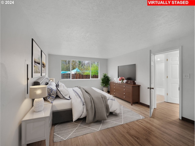 bedroom featuring baseboards, a textured ceiling, and wood finished floors
