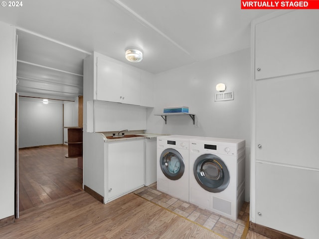 clothes washing area with washer and dryer, a sink, light wood finished floors, and cabinet space