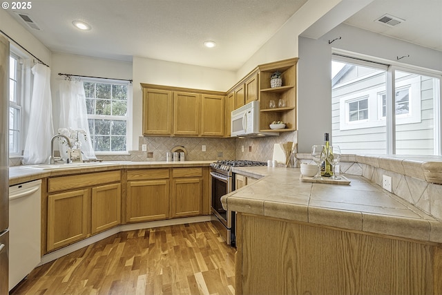 kitchen with light wood-type flooring, white appliances, tile countertops, and backsplash