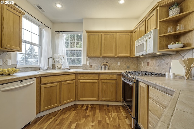 kitchen with tile counters, light hardwood / wood-style floors, white appliances, and sink