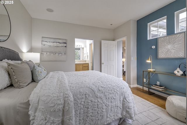 bedroom featuring ensuite bath, light wood-type flooring, and multiple windows