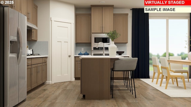 kitchen featuring stainless steel microwave, a center island, fridge with ice dispenser, light countertops, and light wood-style floors