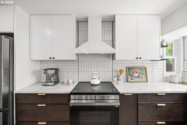 kitchen with wall chimney range hood, stainless steel appliances, dark brown cabinetry, white cabinets, and a textured ceiling