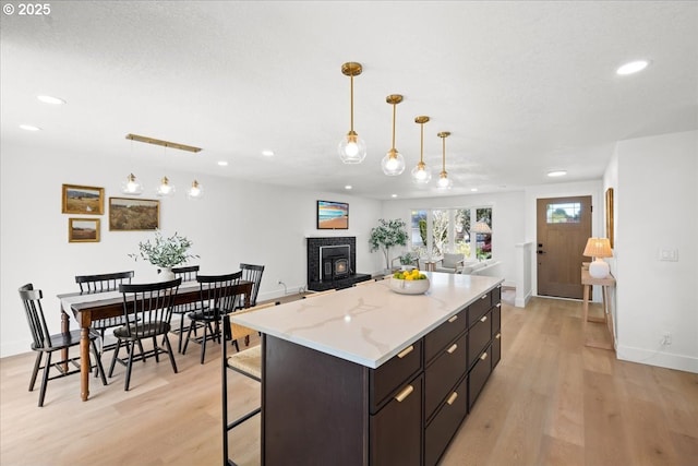 kitchen with light wood-style flooring, recessed lighting, a tiled fireplace, baseboards, and a center island