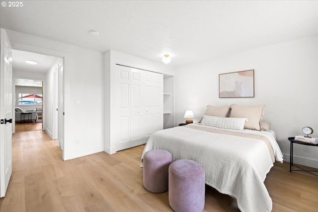 bedroom with light wood-type flooring, baseboards, and a closet