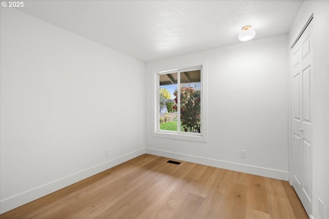 unfurnished room with light wood finished floors, baseboards, and a textured ceiling